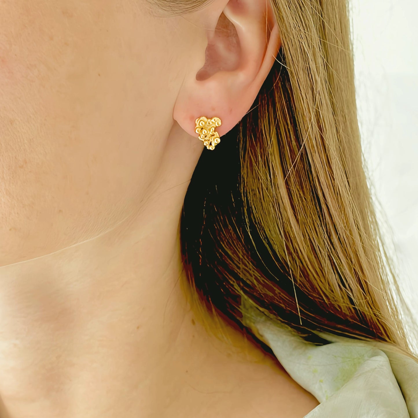 Close-up of a person wearing a gold earring with a blurred background
