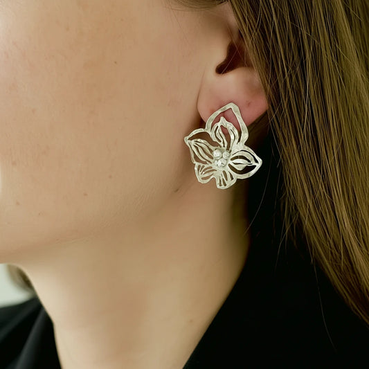 Silver orchid earring worn by a person with blurred background