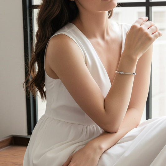 Woman wearing a white dress and a silver bracelet with gemstones on her wrist, sitting indoors with a neutral background