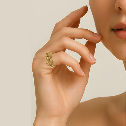 Close-up of a hand wearing a gold-plated textured ring on a neutral background