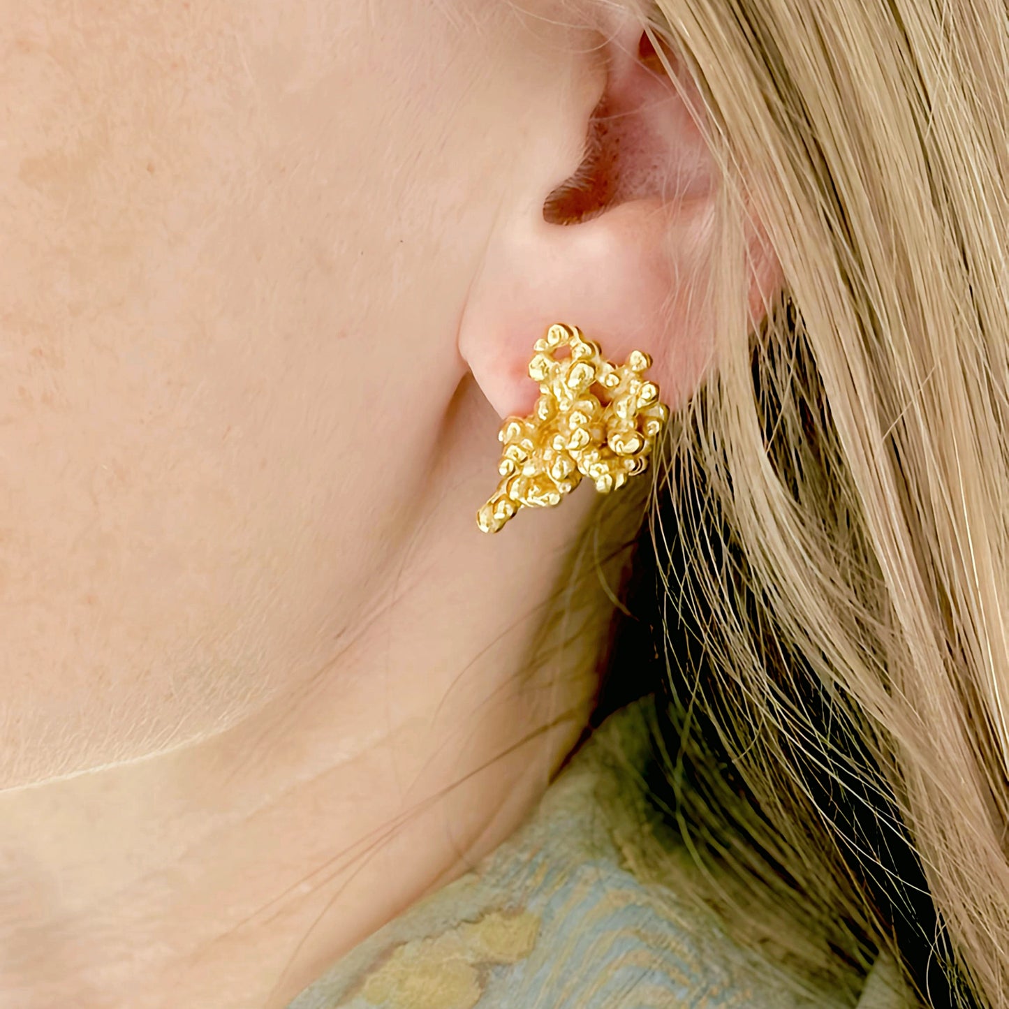 Gold earring worn by a person with blonde hair