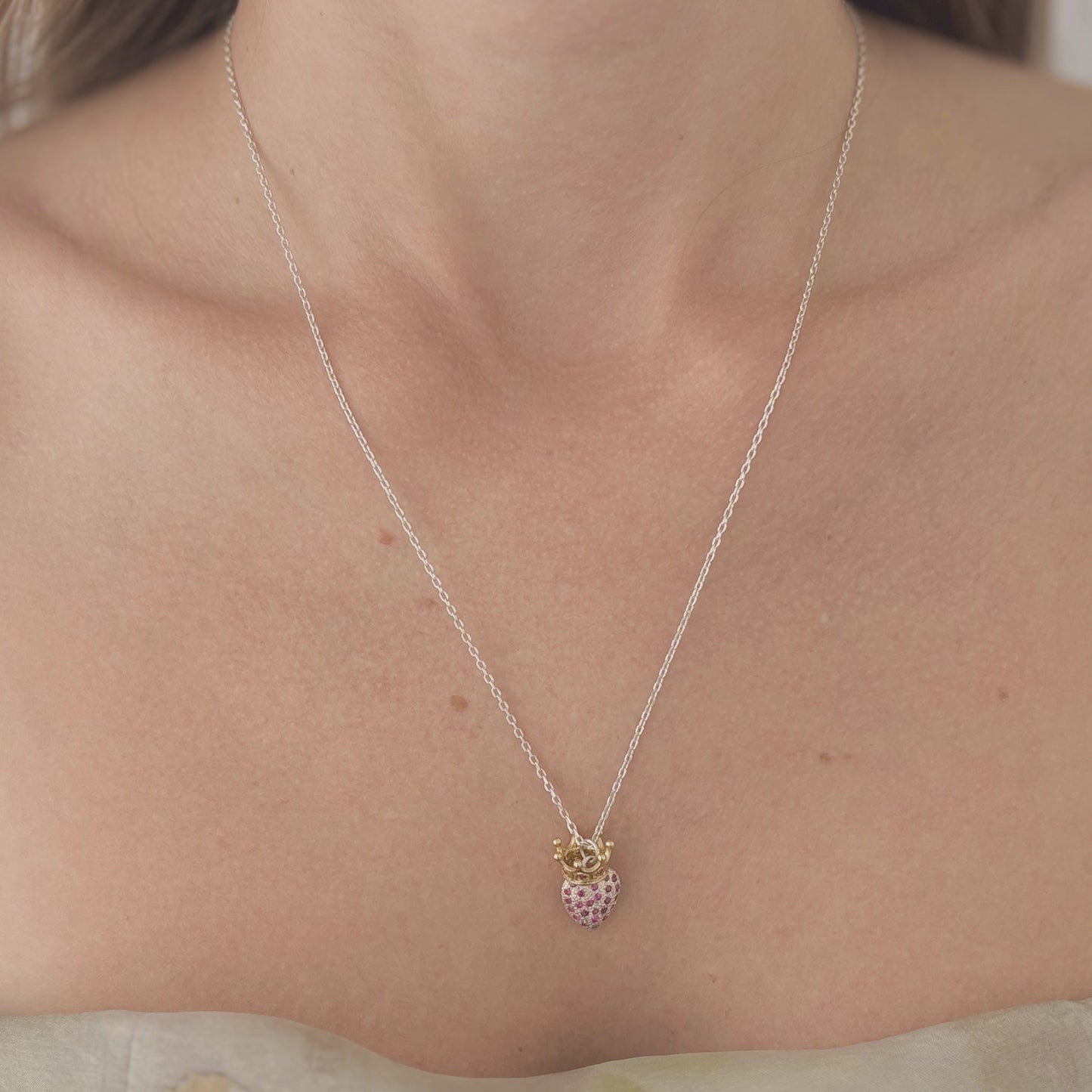 Silver chain with a heart shaped pendant encrusted with red zirconias and golden crown