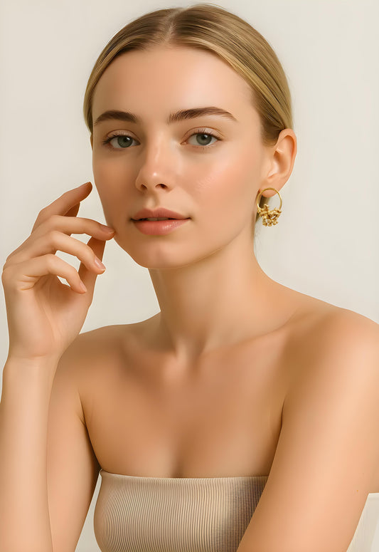 Woman wearing golden hoop stud earrings against a plain background