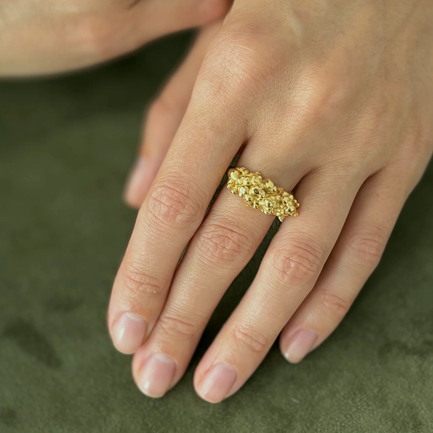 Gold ring on a person's finger against a green fabric background