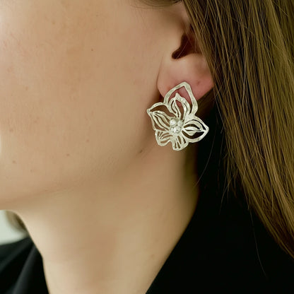 Silver orchid  earring worn by a person with blurred background
