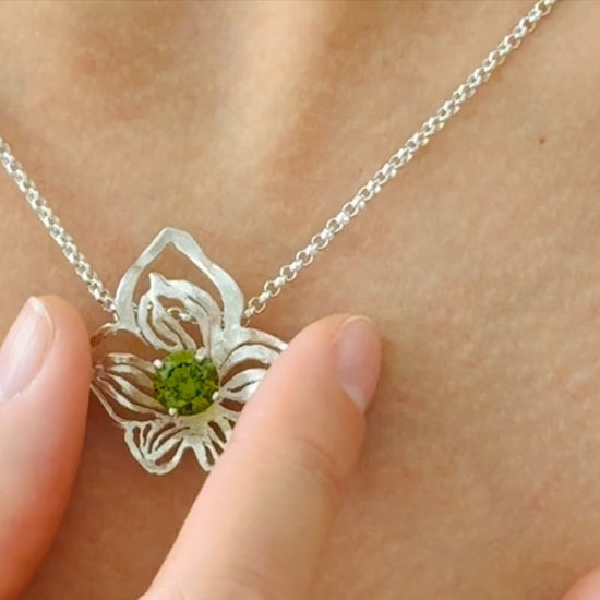 close up of orchid silver pendant with green crystal on silver chain on female model 