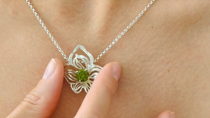 close up of orchid silver pendant with green crystal on silver chain on female model 