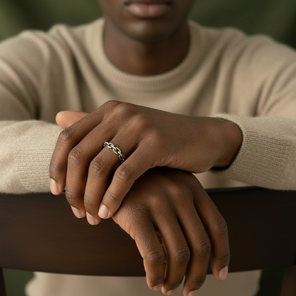 dark skinned model wearing a bege sweater is sitting on a chair and showing his hands and he is wearing a silver chain ring