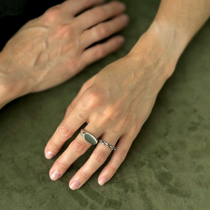 female hands on green velvet background wearing two silver rings
