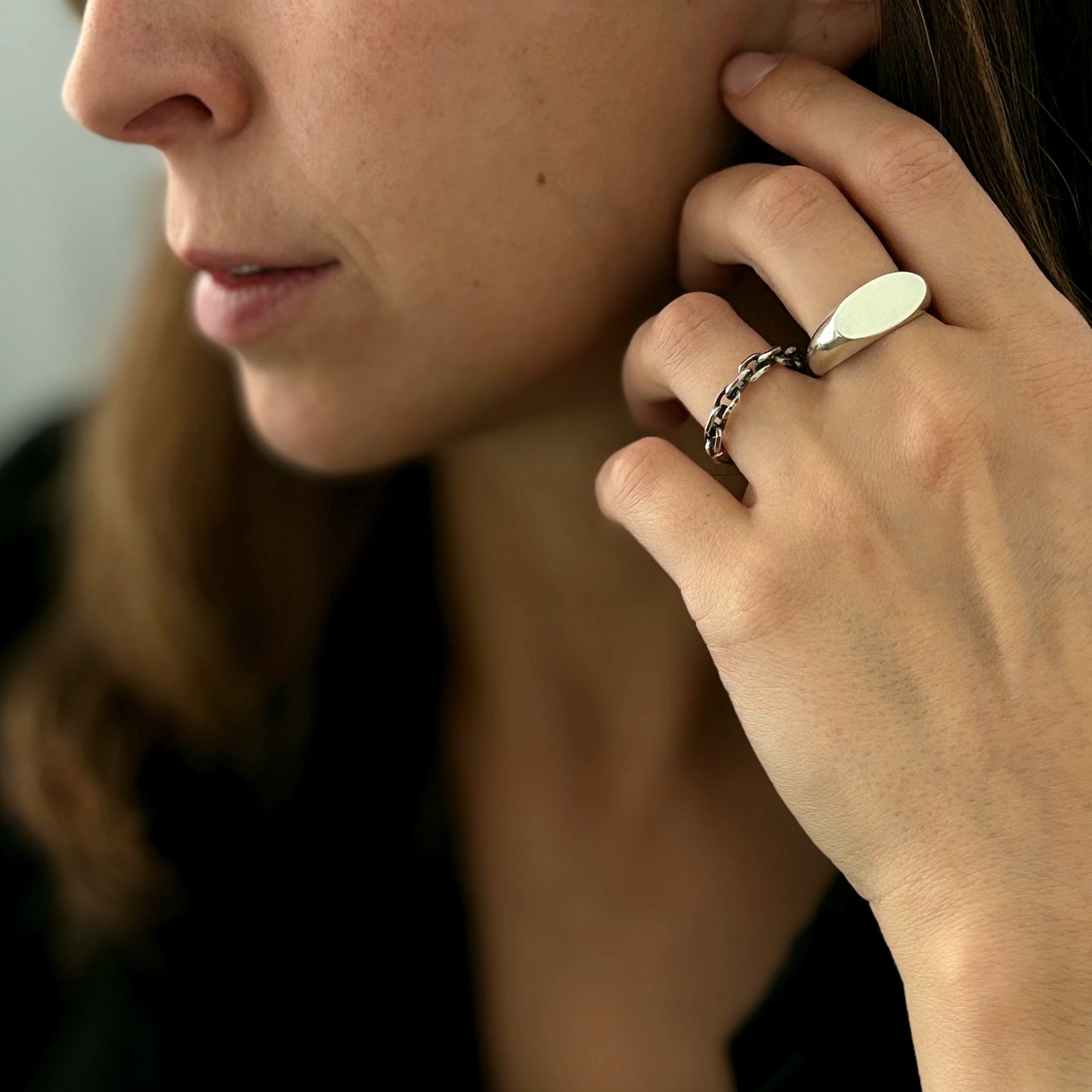 a female holding her hand close to her face and on her hand she has two silver rings: signet and chain
